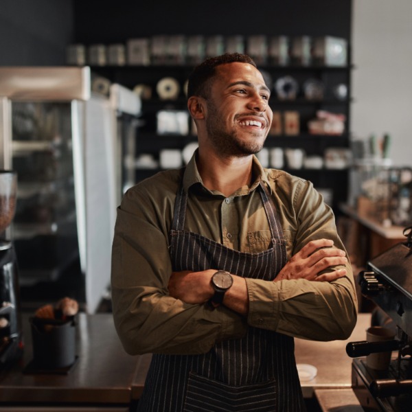 isang nakangiting binatang nakasuot ng apron na nakatayo sa harap ng espresso machine sa isang malayang coffee shop